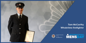 Firefighter Tom McCarthy with his certificate in front of a grey background with the Service crest